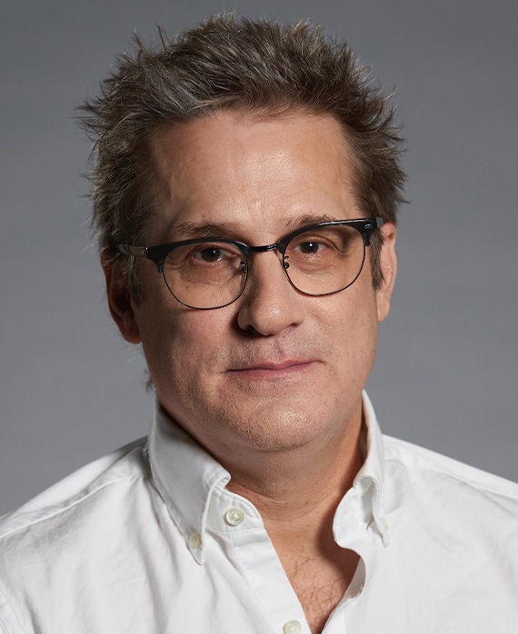Paul Simms headshot wearing glasses and a white button down shirt.