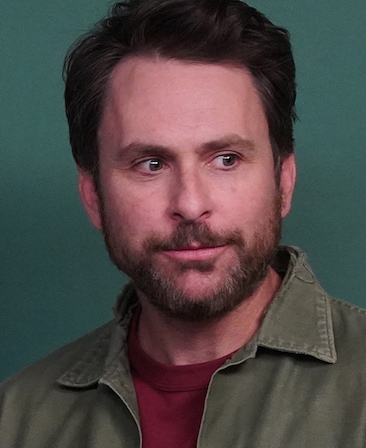 Charlie Day headshot wearing a red shirt and green jacket.