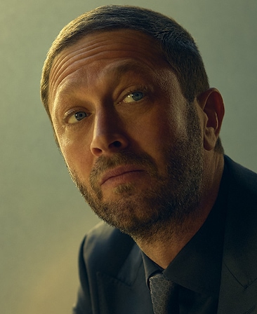 Ebon Moss-Bachrach headshot wearing a navy suit and tie.