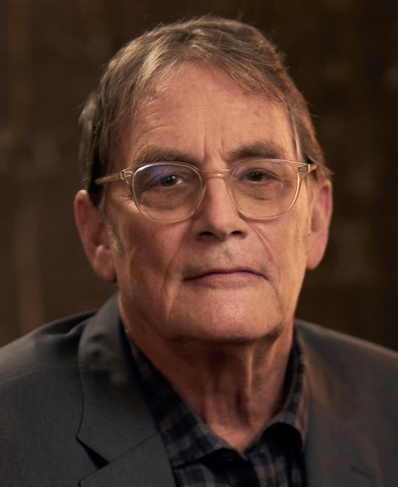 Michael Dinner headshot wearing a shirt and suit jacket with clear glasses.