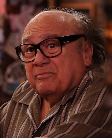 Danny DeVito headshot wearing a stripped multi-colored button up and glasses.