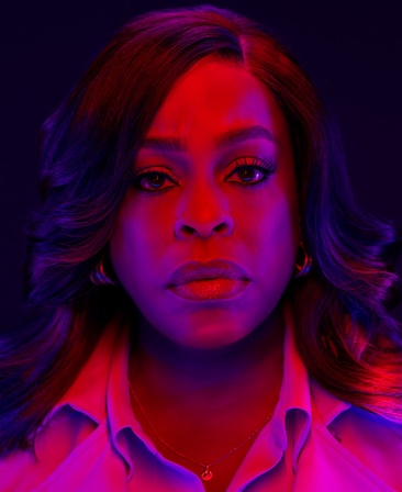 Niecy Nash-Betts as Lois Tryon in FX's Grotesquerie in a button up and coat with pink and blue lights shone on her face.
