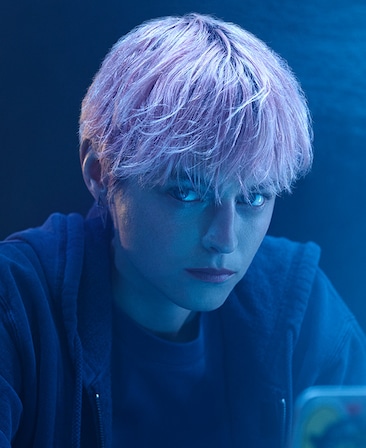Emma Corrin headshot with pink hair, wearing a black hoodie