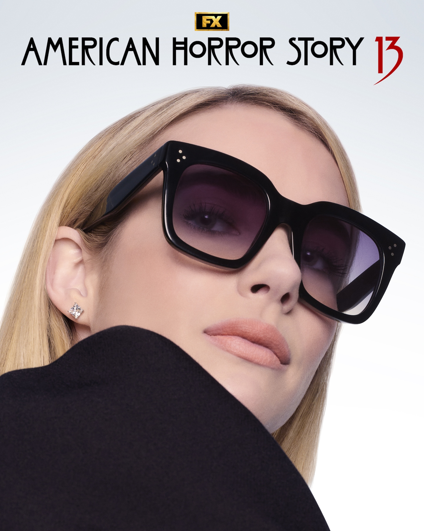 Emma Roberts wearing black sunglasses, diamond earrings and a black top looking over her shoulder.