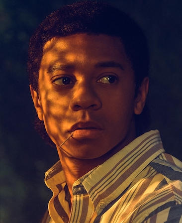 DeRon Horton headshot in shadows with light shining on face and biting on toothpick from American Horror Story 1984