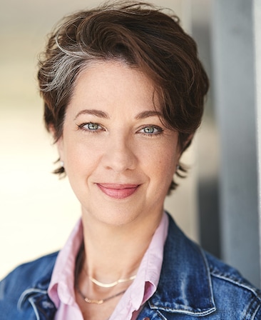 Melanie Marnich headshot wearing a denim jacket and a pink shirt
