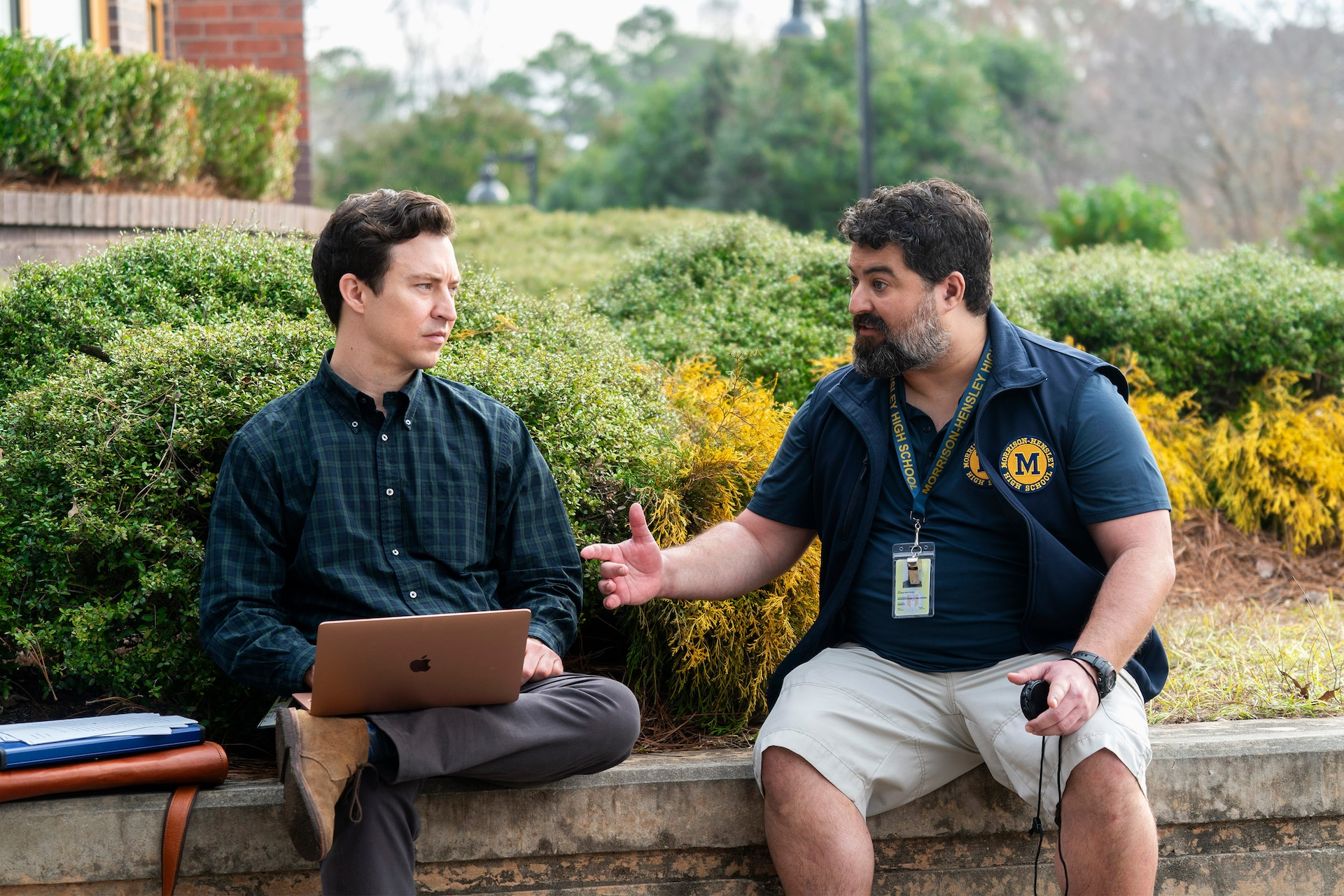 Evan and Markie sitting on a ledge in front of a bush.