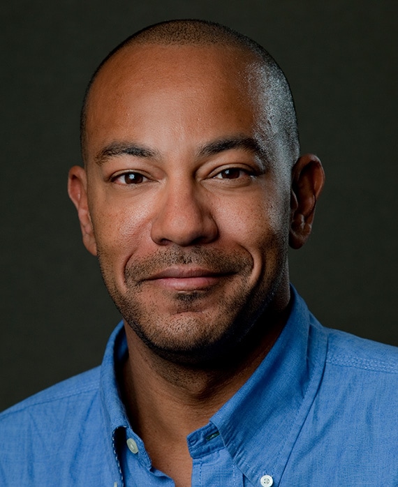 Carl Beverly headshot wearing a blue button down in front of a black background.