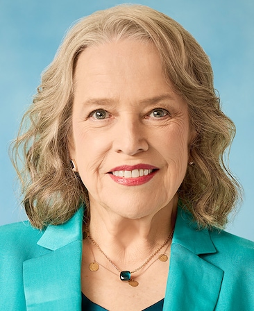 Kathy Bates headshot wearing a blue suit with blue background for AHS: 13