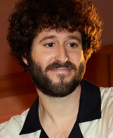 Dave Burd wearing a white shirt with a black collar smiling toward the ground