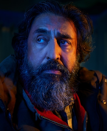 Javed Khan headshot wearing a puffy jacket sitting in the dark
