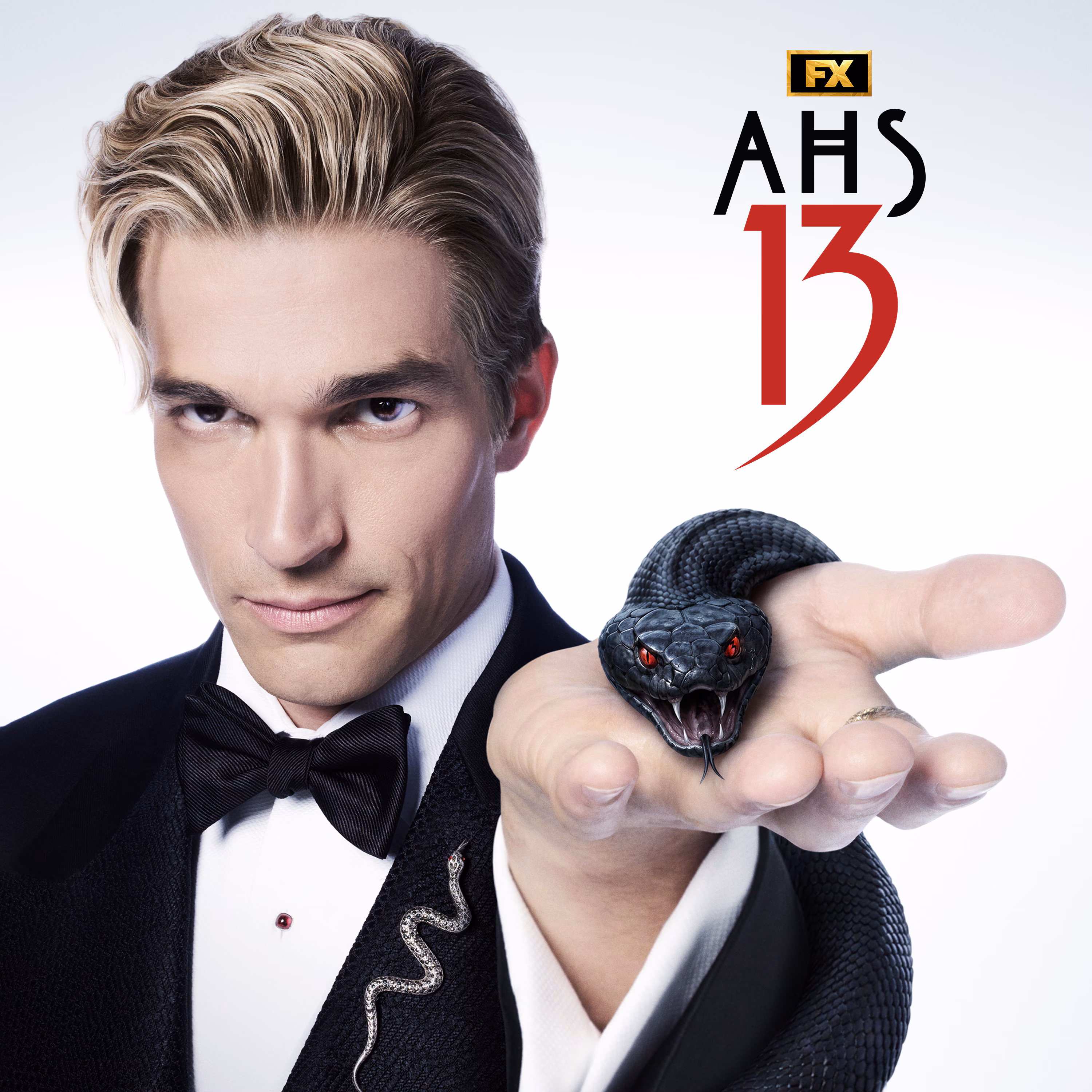 Paul Anthony Kelly in FX's AHS: 13 wearing a tuxedo, holding a black, red eyed snaked in his palm.