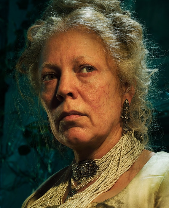Olivia Colman headshot with string of small pearl necklaces connected by diamond pendant, with hair messily up in bun