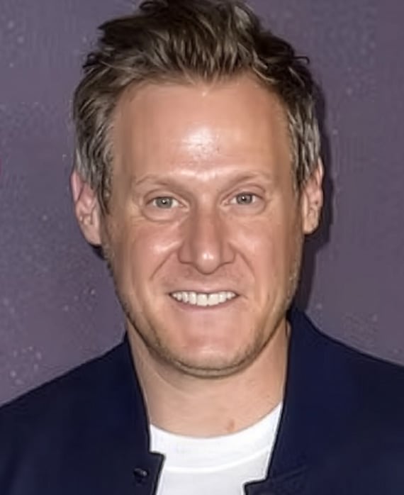 Headshot of executive producer Trevor Engelson wearing a white shirt and blue button up with purple background.