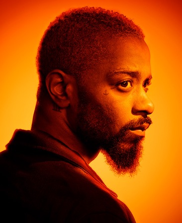 Headshot of LaKeith Stanfield looking over his shoulder with heavy orange sunset lighting over face and background