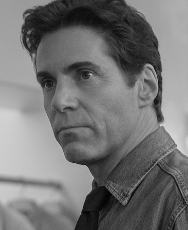 Black and white headshot of Alessandro Nivola as Calvin Klein in FX's Love Story wearing a denim jacket.
