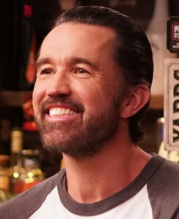 Rob McElhenney headshot wearing a white and grey shirt inside of Paddy's pub.