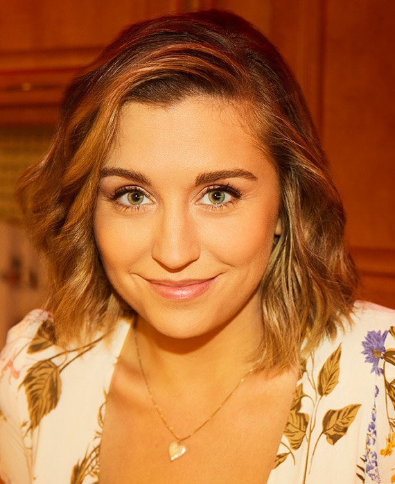 Taylor Misiak smiling and wearing a floral top and gold necklace for FX's DAVE