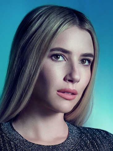 Emma Roberts headshot wearing a gray knit top standing against a blue background for AHS: Delicate