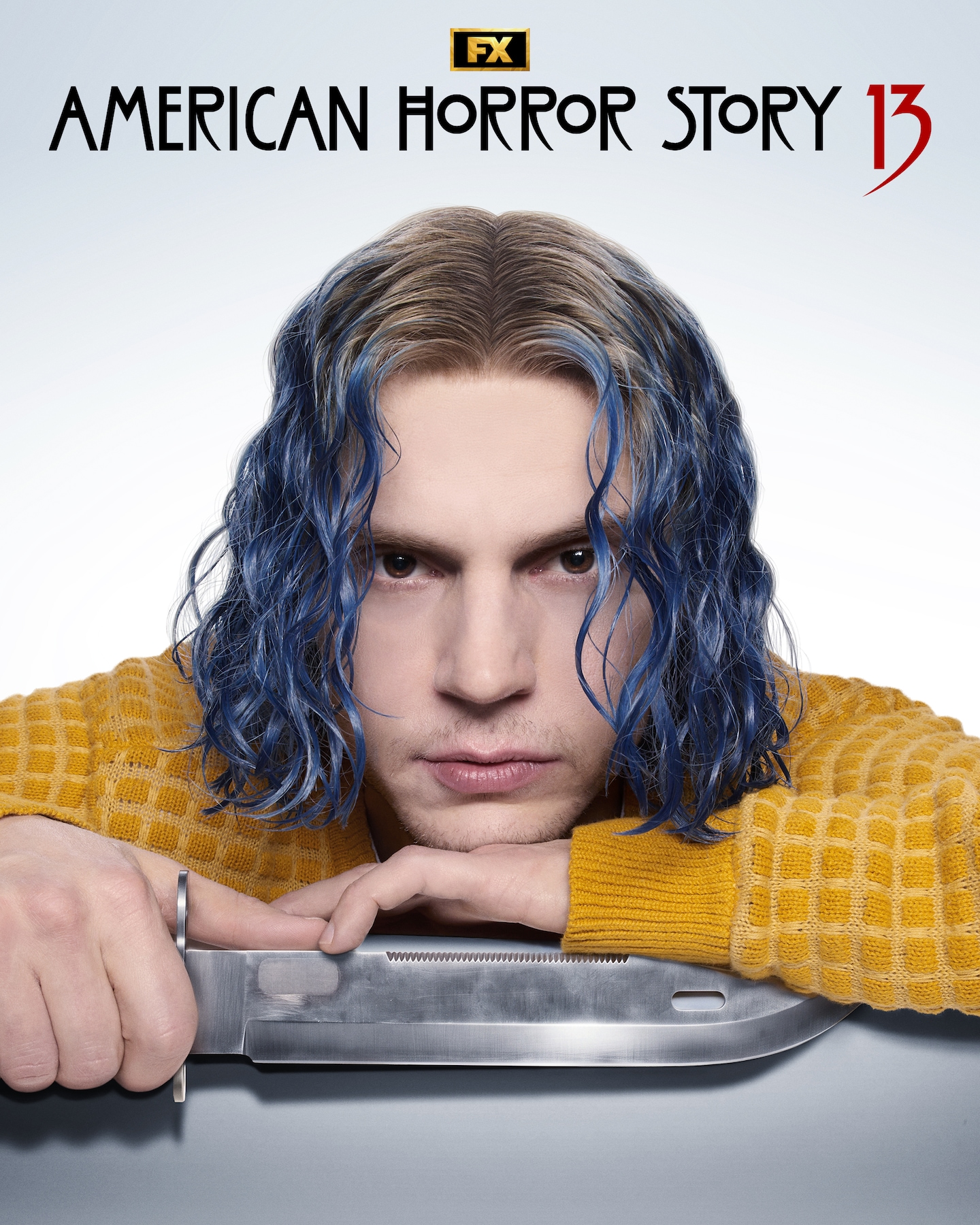 Evan Peters with blue hair and a yellow sweater holding a knife.
