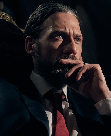 Adam Rayner headshot wearing a suit and placing his hand on his month
