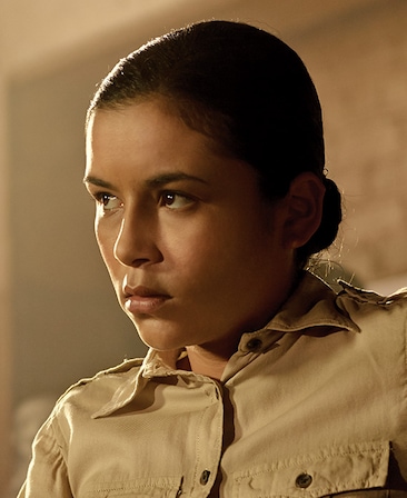 Emily Rios headshot in beige cargo uniform with hair in bun, looking to the side with sun shining on face