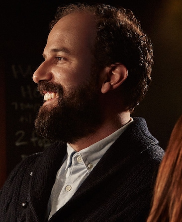 Brett Gelman headshot wearing a gray button up shirt and black jacket