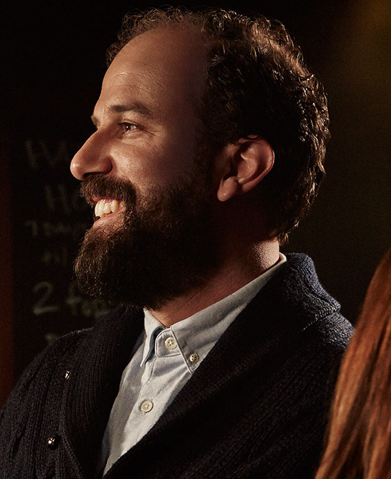 Brett Gelman headshot wearing a gray button up shirt and black jacket