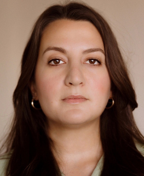 Sarina Roma headshot wearing gold hoop earrings with a beige background
