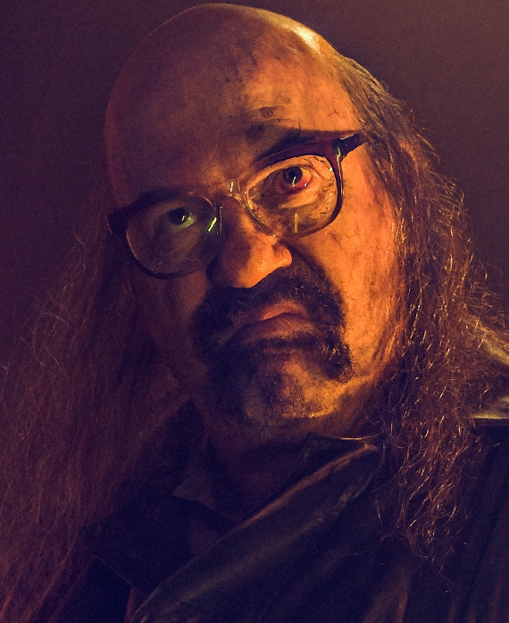 John Carroll Lynch headshot with grown out mullet and bald top and dirt on face from American Horror Story 1984