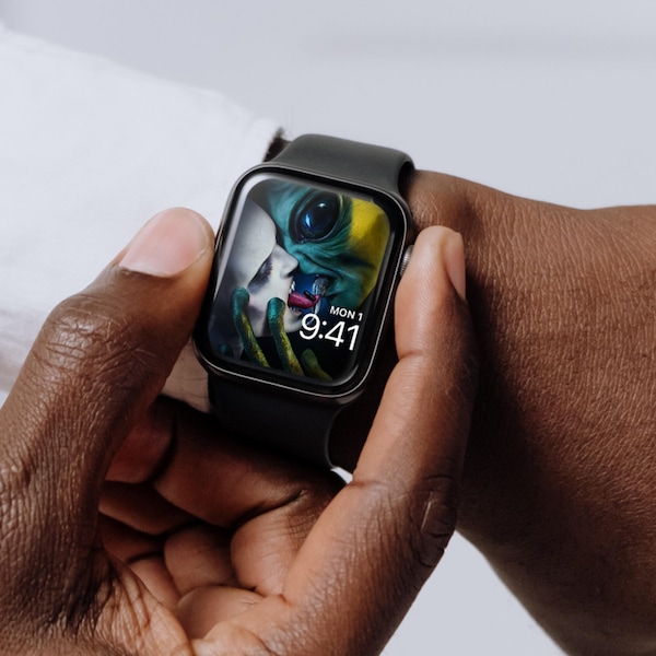 Man wearing Apple Watch with lock screen of alien and monster swapping black pill with tongues from FX's AHS Double Feature
