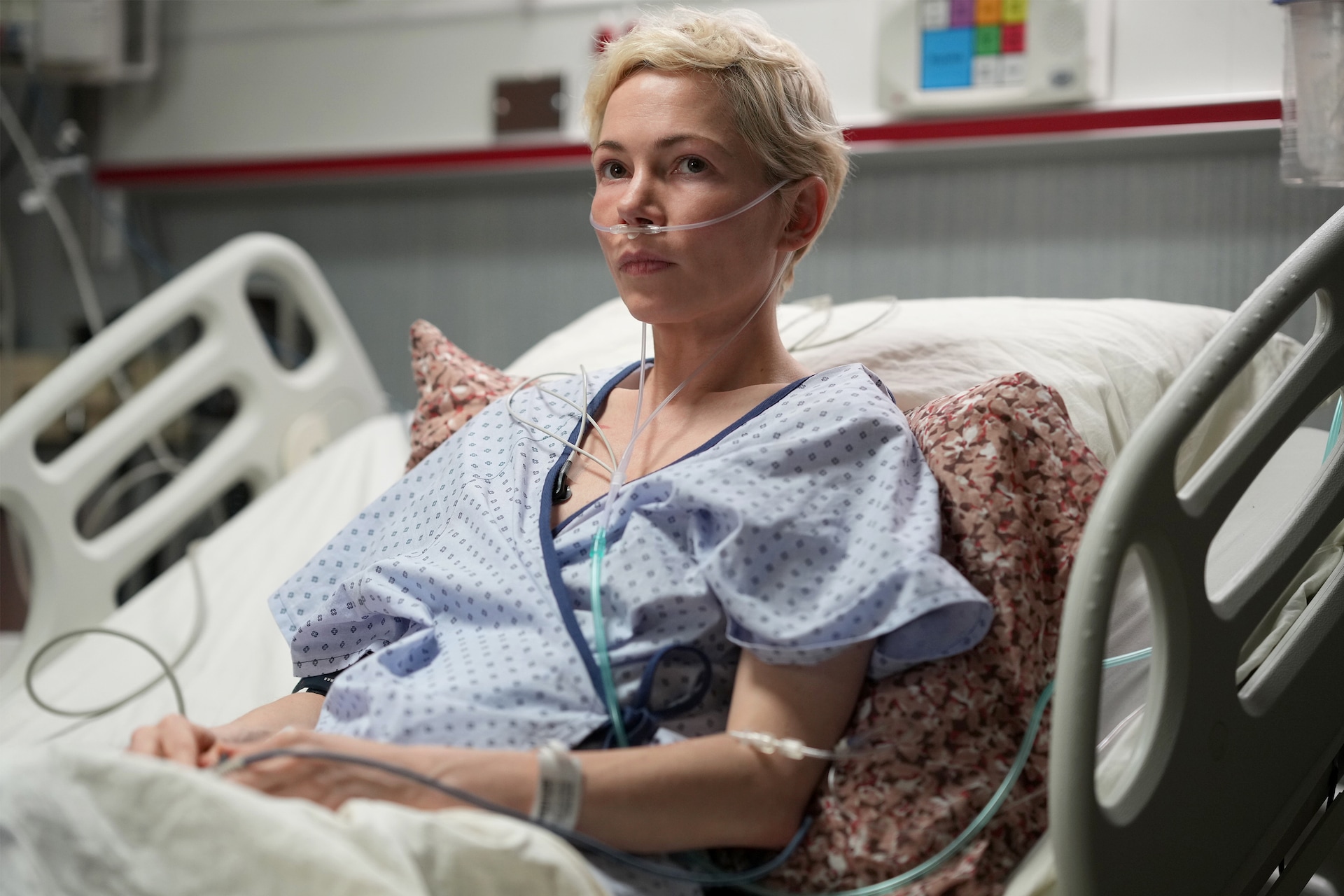 Molly sitting in a hospital bed wearing a blue hospital gown and breathing tubes in her nose in FX's Dying for Sex