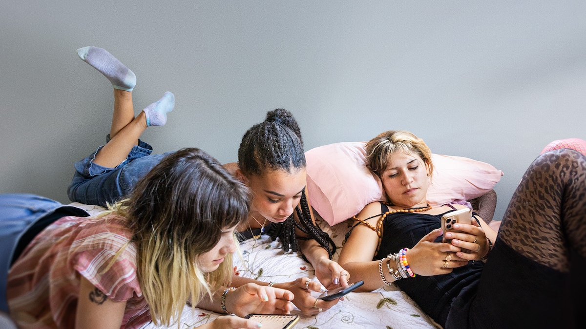 3 girls laying on a bed while looking at their phones.