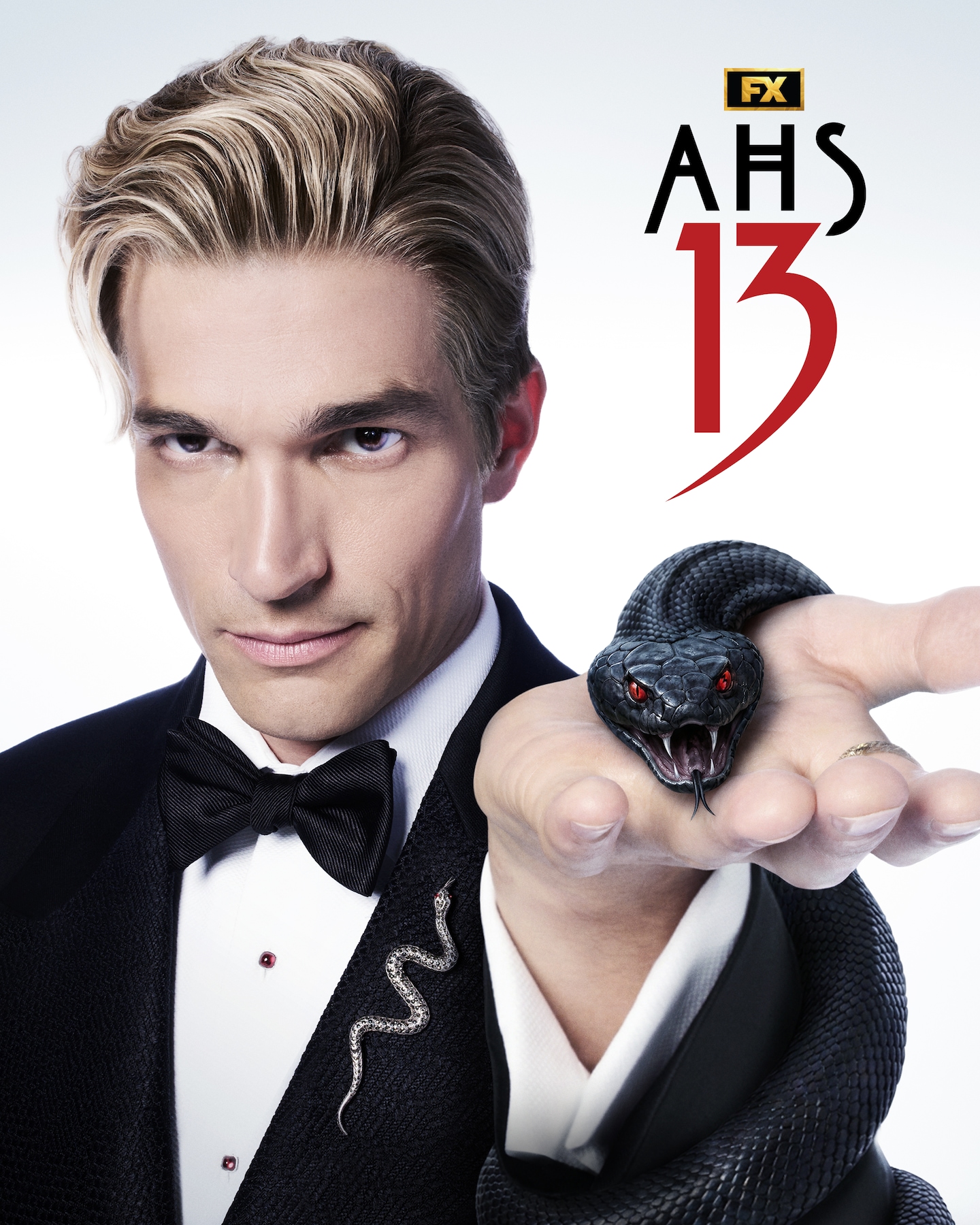 Paul Anthony Kelly wearing a suit with a snake pin, holding a black snake with red eyes.