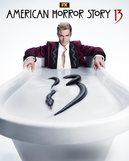 Paul Anthony Kelly wearing a maroon suit with a black snake detailing in a bathtub of white liquid with a black snake with red eyes contorted to spell "13."