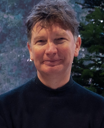 Black and white Andrew Macdonald headshot in black high neck top with painting in background