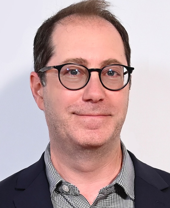 Craig Silverstein headshot wearing a checkered button up and navy blue suit