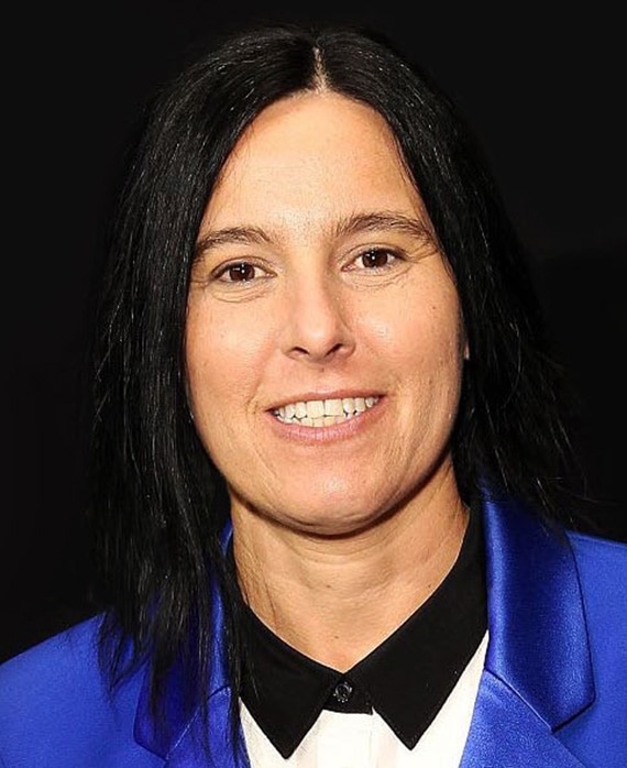 Andrea Sperling headshot wearing a blue suit jacket standing against a black backdrop