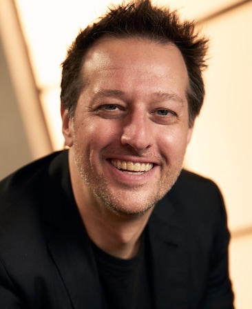 Dave Andron headshot wearing a black shirt, near a window.