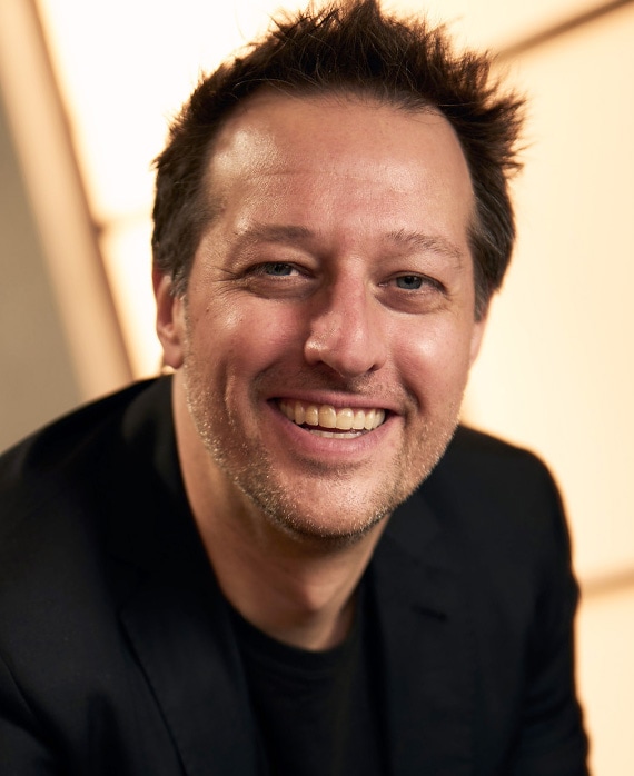 Dave Andron headshot wearing a black shirt, near a window.