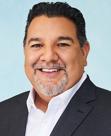 Headshot of executive producer of FX's Necaxa, Cris Abrego, wearing a white collared button down and a grey suit.
